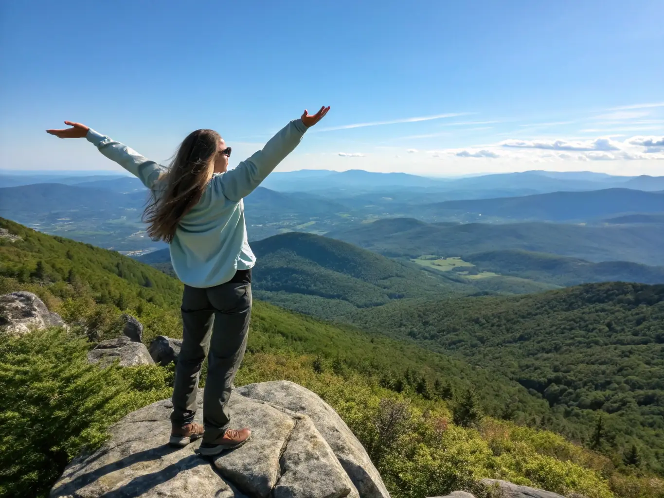 A hiker is shown reaching the summit of a mountain, arms raised in triumph, with a panoramic view of rolling hills and valleys in the background. The image conveys a sense of accomplishment and well-being.